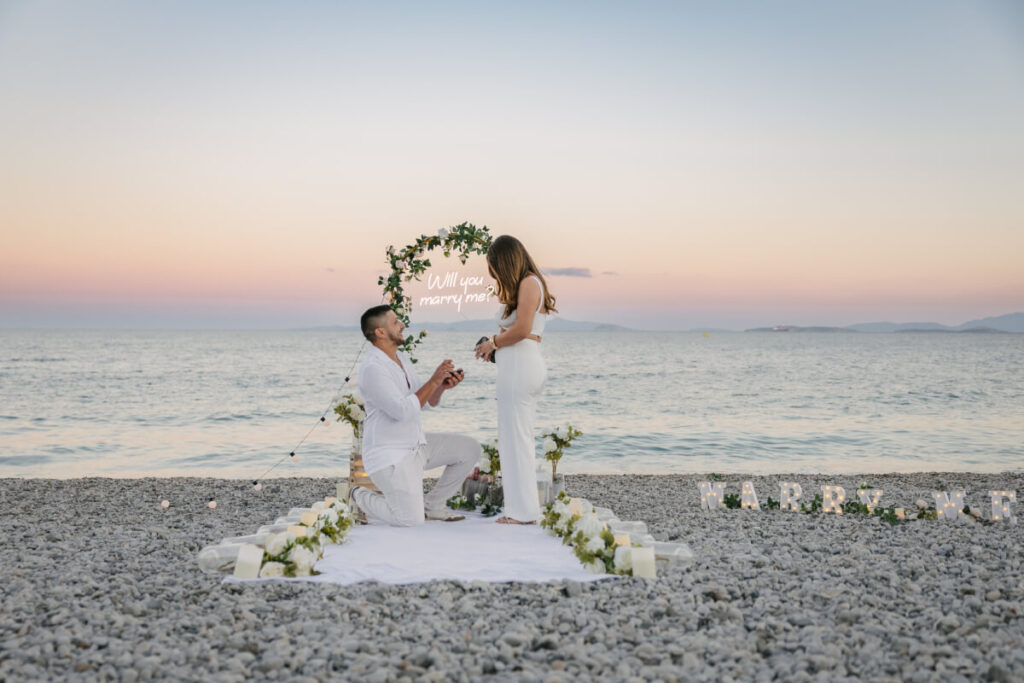 הצעת נישואין רומנטית באתונה על חוף הים בשקיעה עם תפאורת Marry Me ונרות